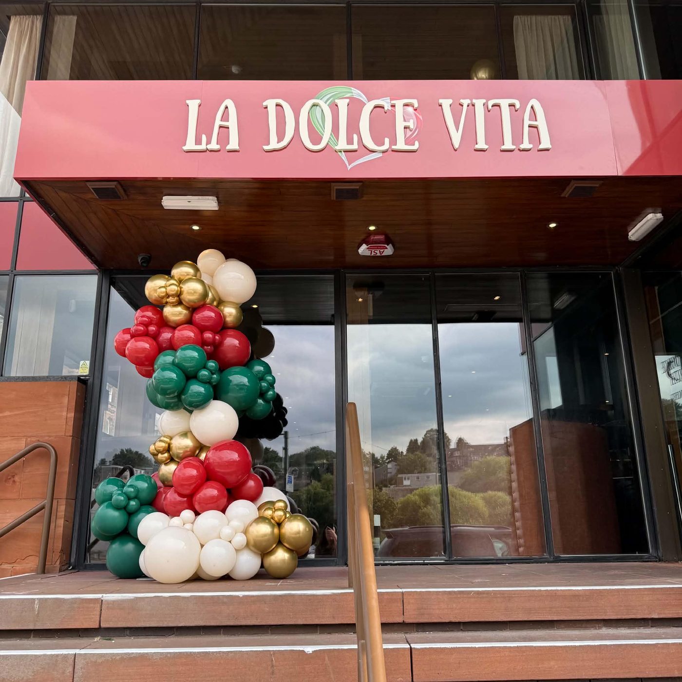 The La Dolce Vita sign on the Whitesands frontage: cream lettering and the tricolour heart on a red fascia, above the steps up from the street